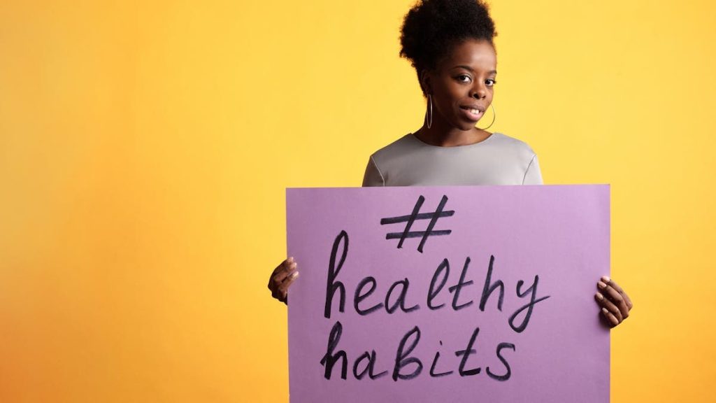 Portrait of a woman holding a healthy habits sign, set against a vibrant yellow background.
